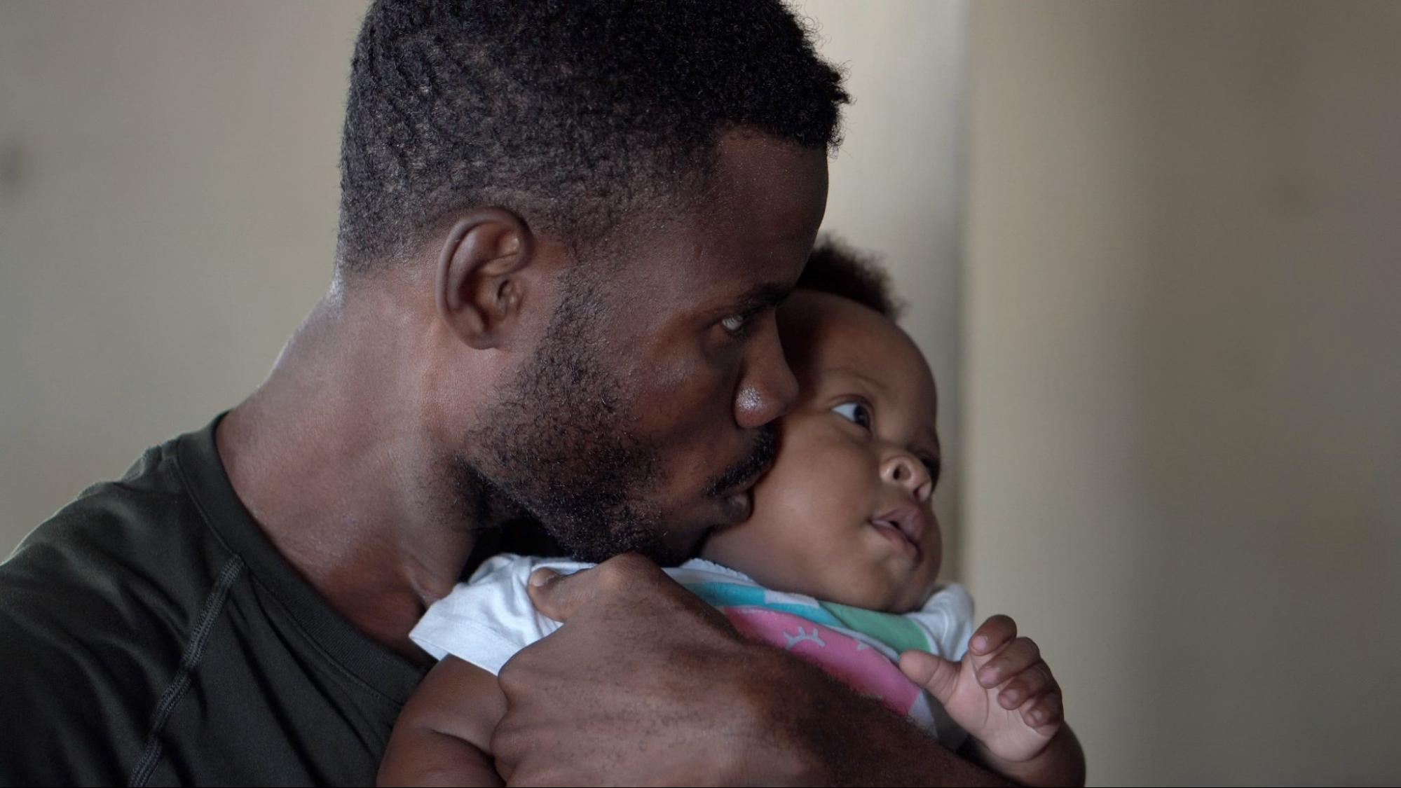 A father embraces and kisses his young child on the cheek.