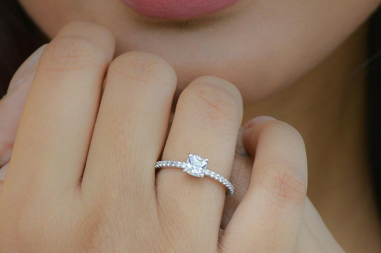 a woman’s hand raised to her chin and adorned with a side stone engagement ring.