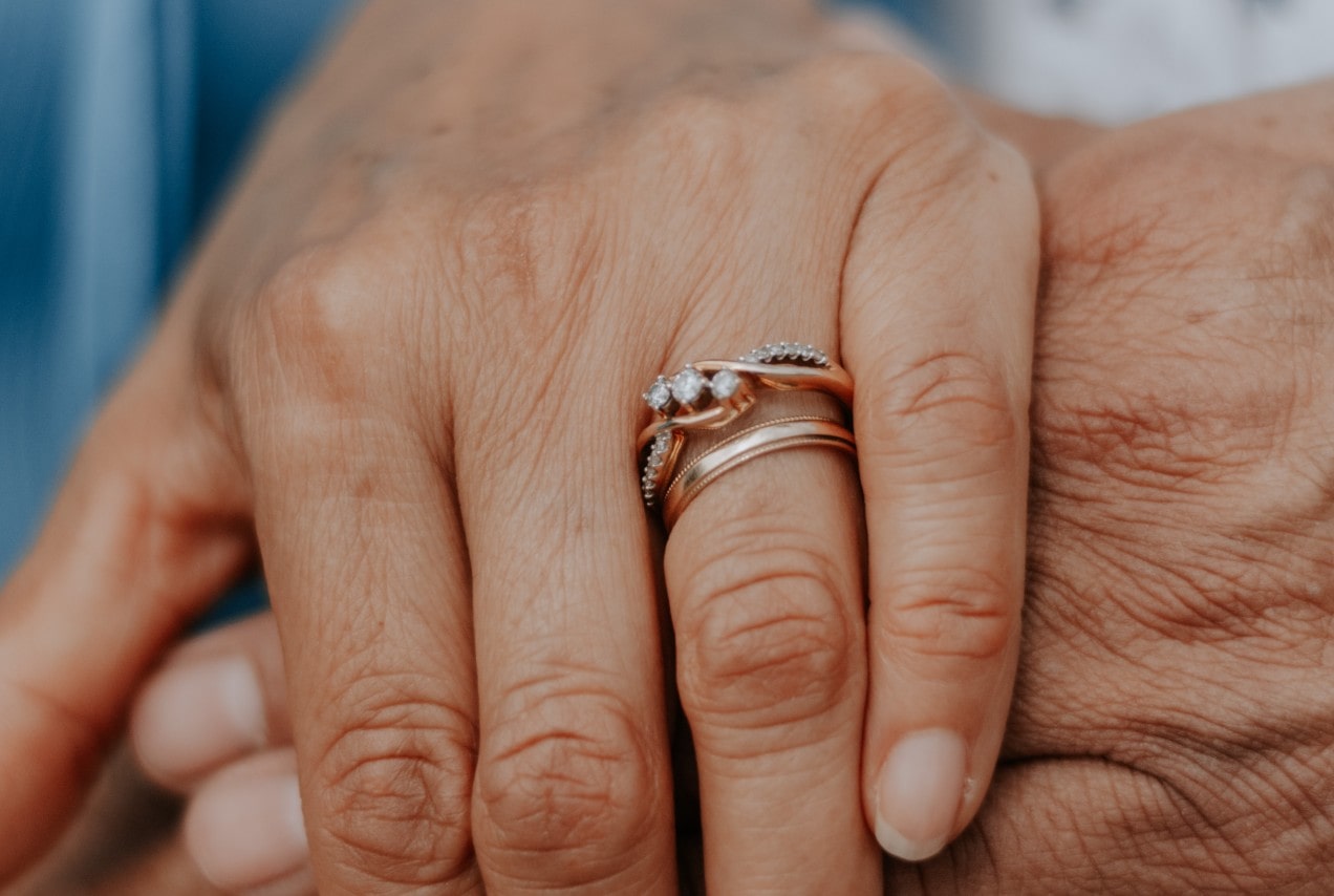 a pair of hands embracing, one adorned with a rose gold engagement ring and wedding band.