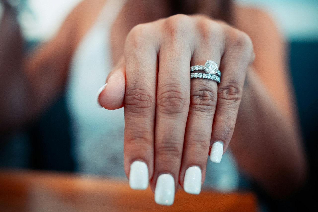 a woman’s outstretched hand showing off a silver engagement ring and diamond wedding band.