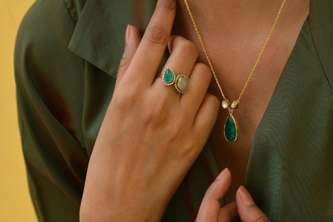 A close-up image of a woman wearing a toi et moi fashion ring and gemstone necklace.