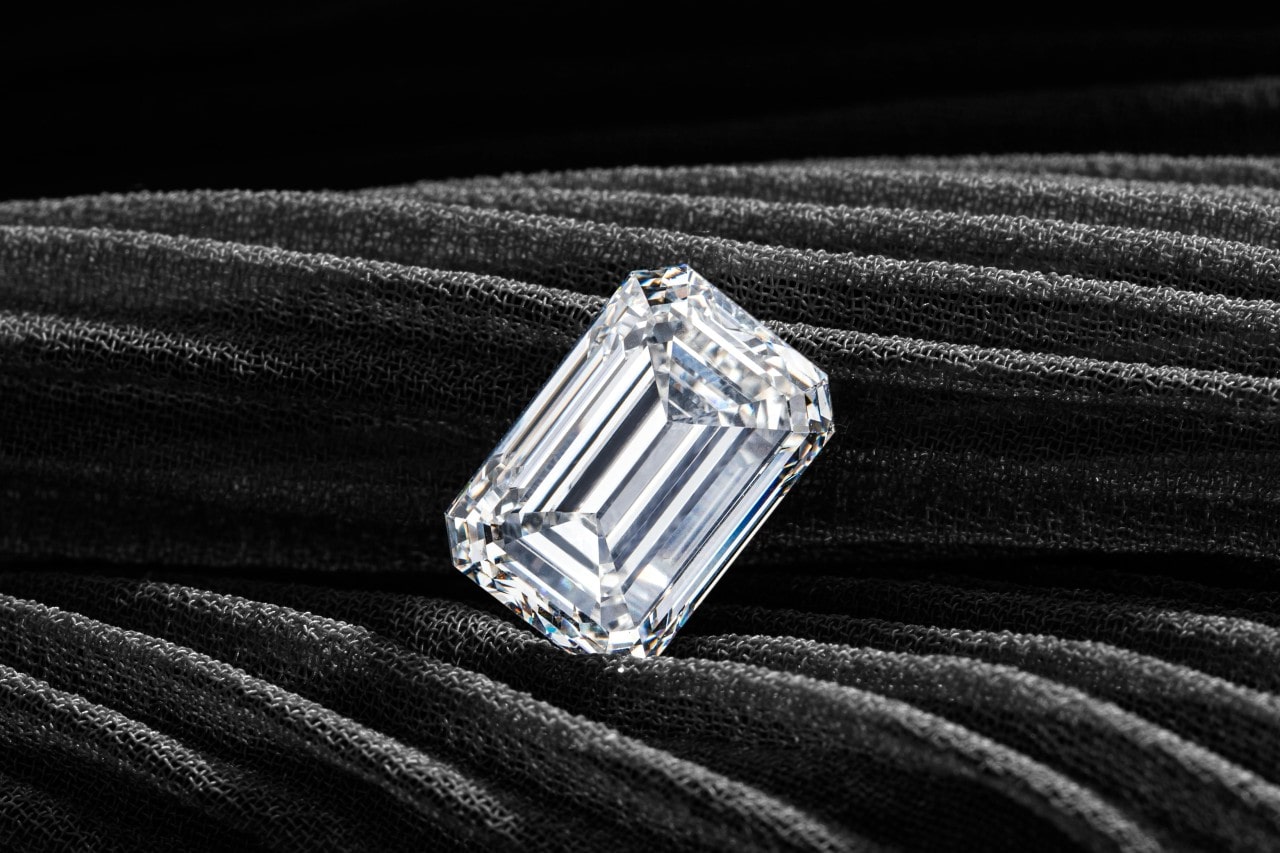 A stunning emerald-cut diamond on a dark fabric background.