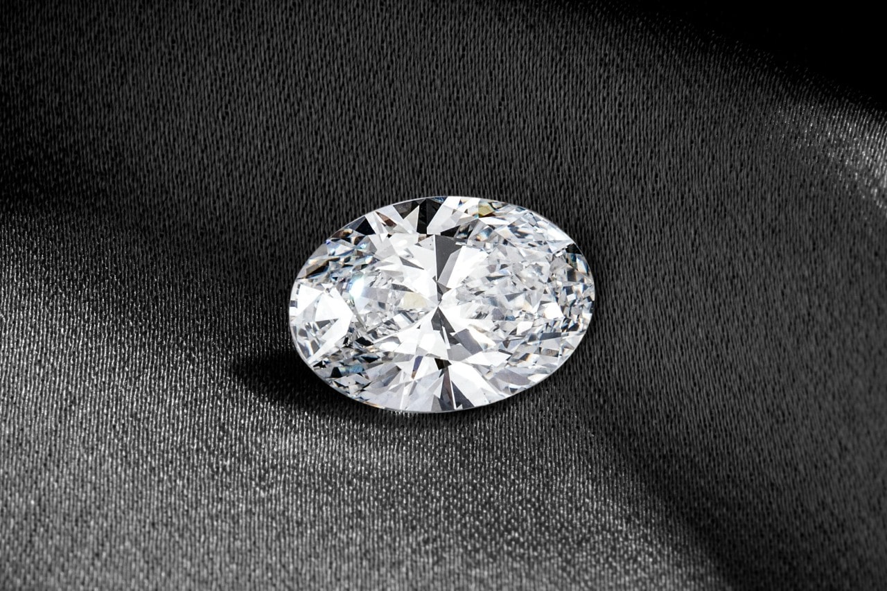 A single oval-cut diamond on a dark fabric background.