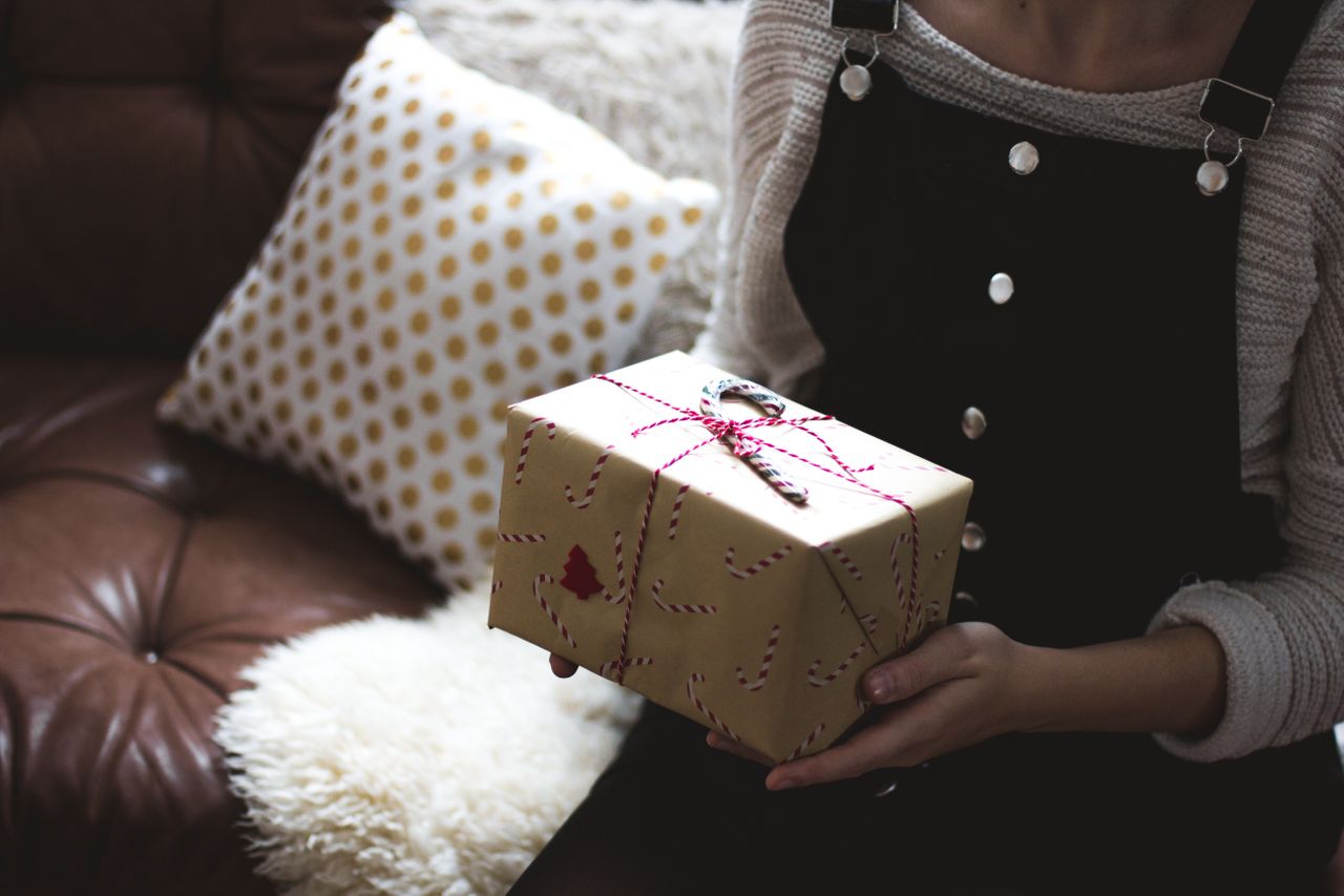 A close-up of a woman holding a wrapped Christmas gift tied with ribbon, holding a candy cane.