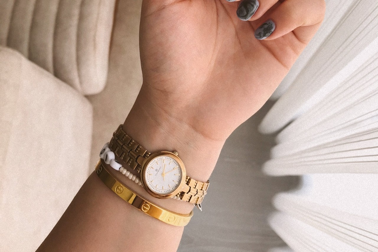 a woman’s wrist wearing a yellow gold watch and two bracelets