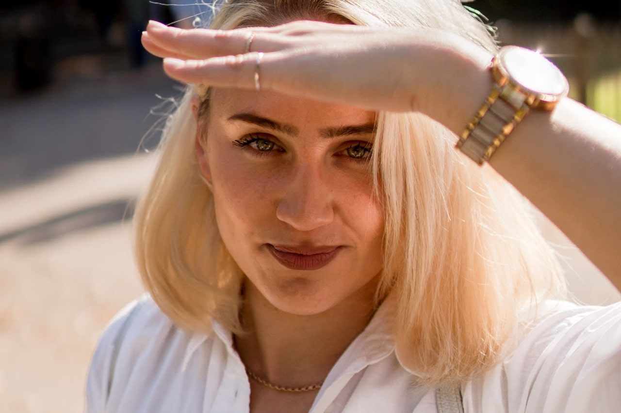 a woman shielding her eyes from the sun, wearing a watch and jewelry