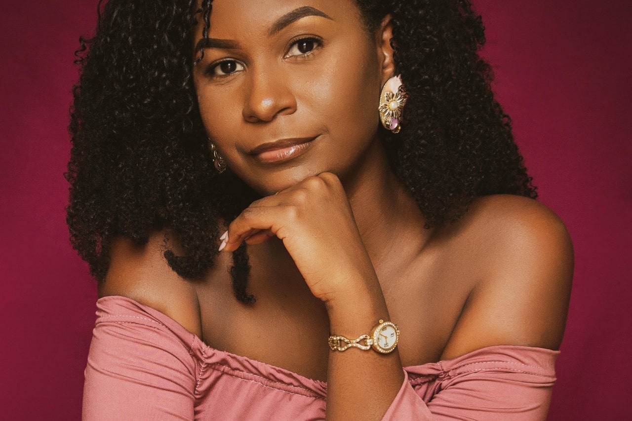 a woman with her hand under chin wearing a decorative watch and earrings