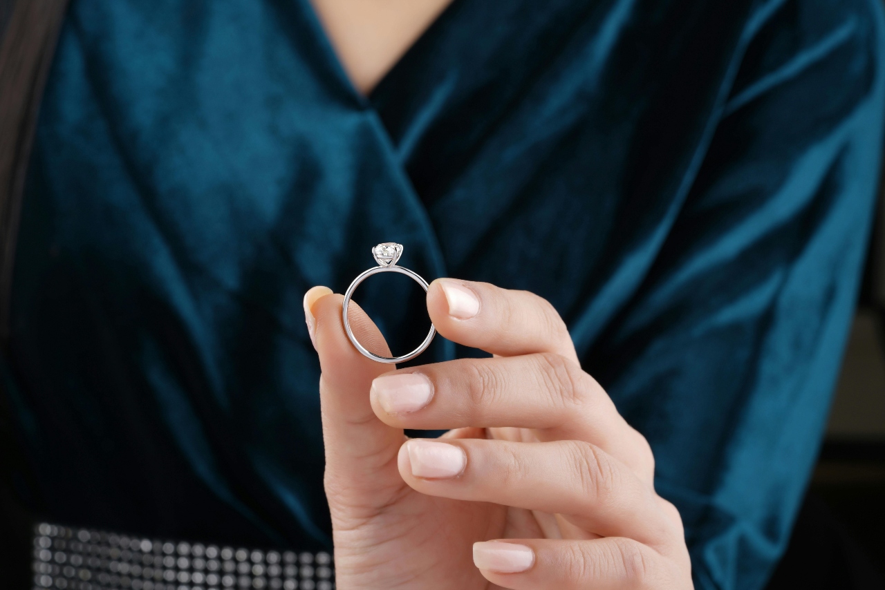 a woman’s hand holding a solitaire engagement ring and wearing a teal top