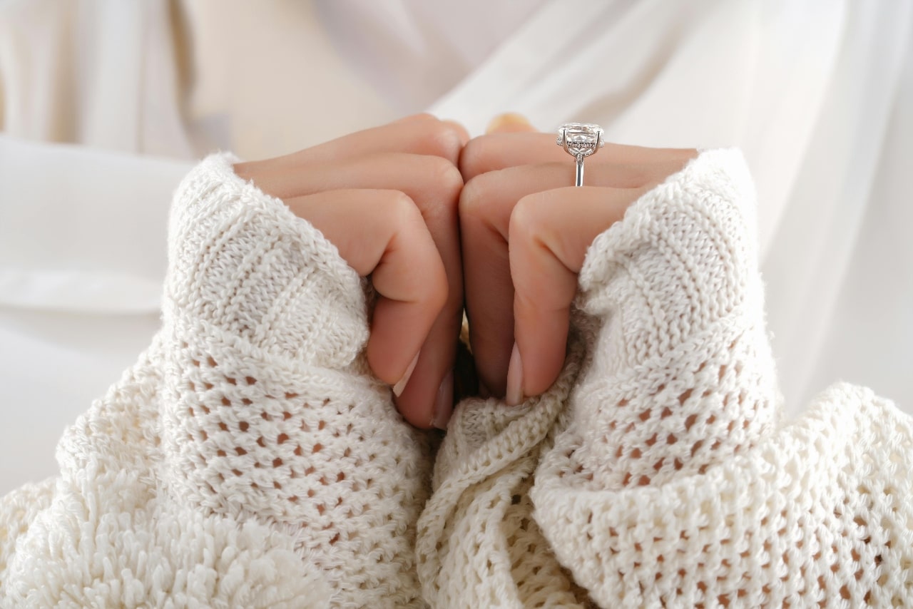 a woman’s hands and wrists adorned with chunky white sweater sleeves and white gold engagement ring