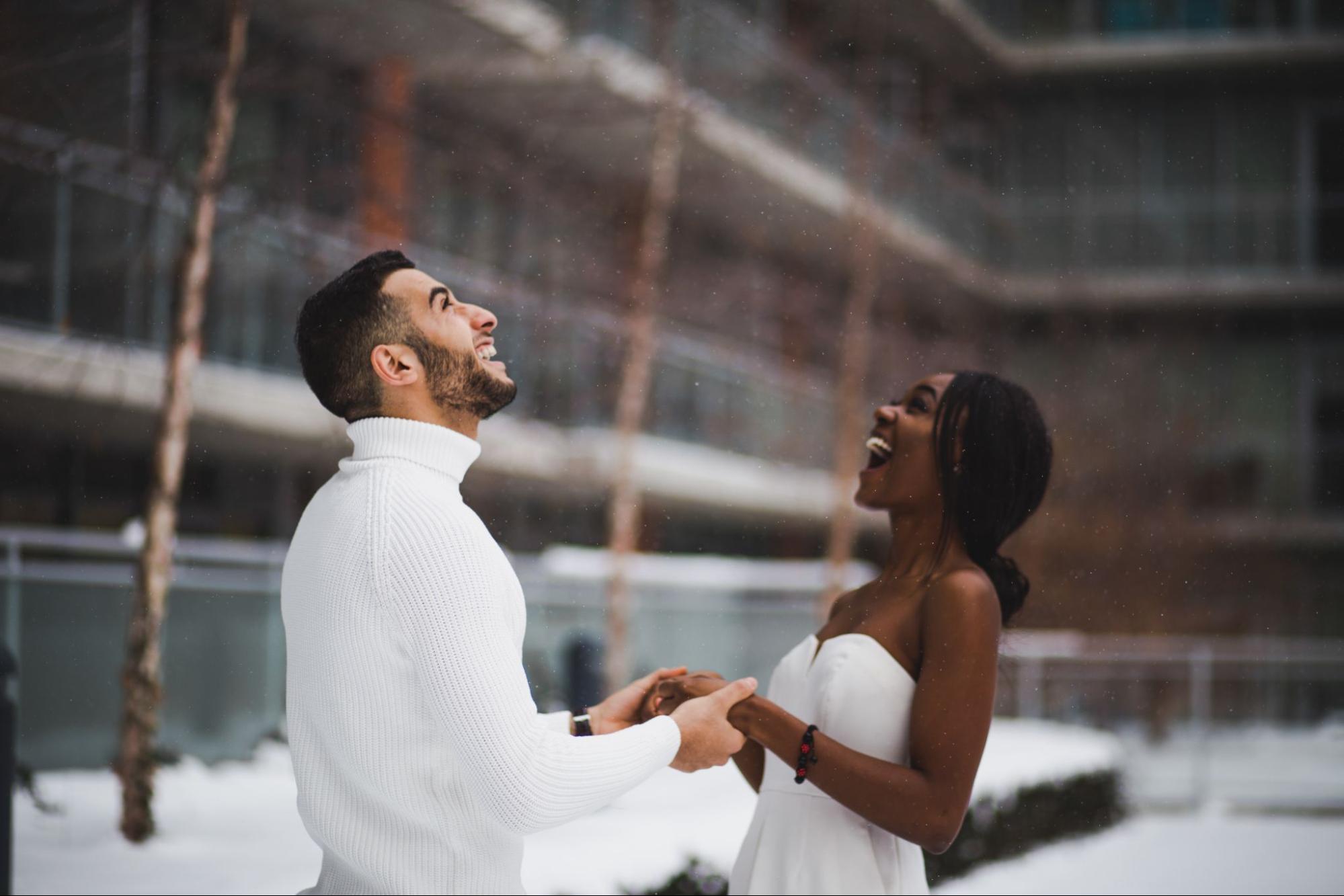 A recently engaged couple holding hands as snow begins to fall.