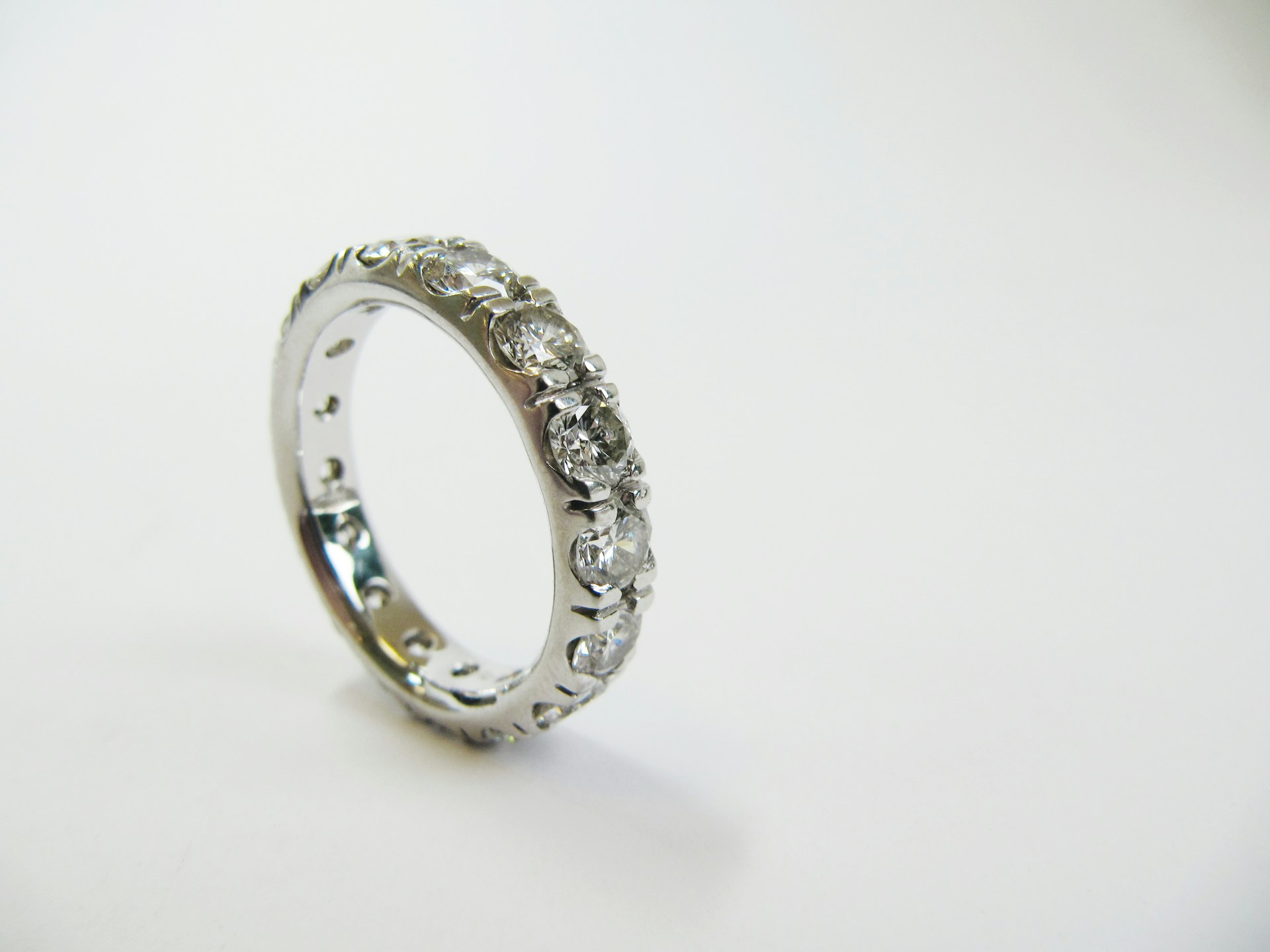 A white gold diamond eternity wedding band standing on its side on a white surface