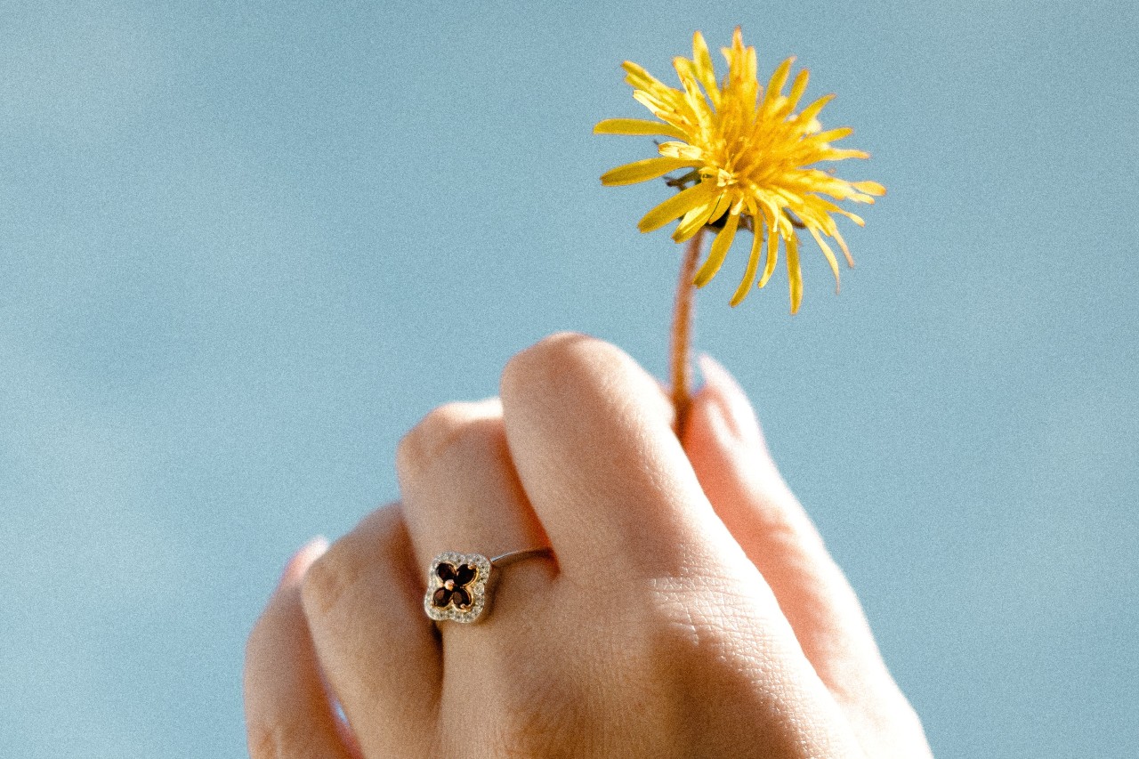 A woman wearing a ruby and diamond ring while holding dandelion flower