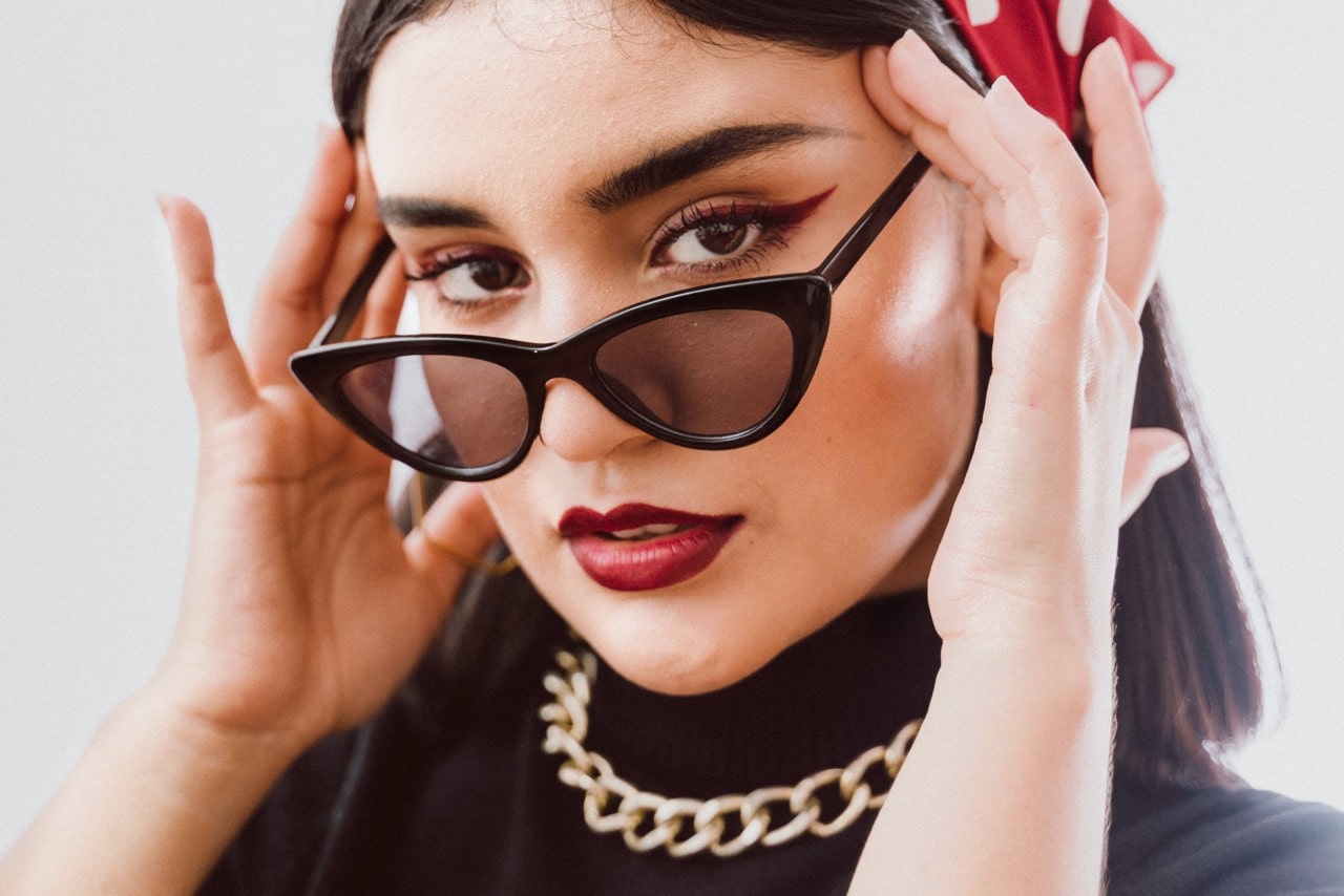 A woman wearing black sunglasses along with matching red lipsticks and red eyeliner along with a red and white polka dot bandana.