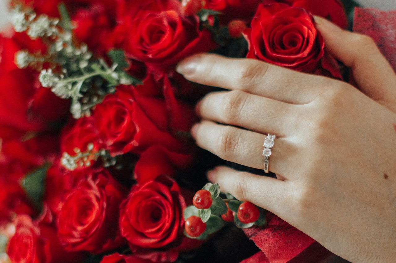 A woman wearing a three stone engagement ring with her hand resting on a boutique of bright red roses