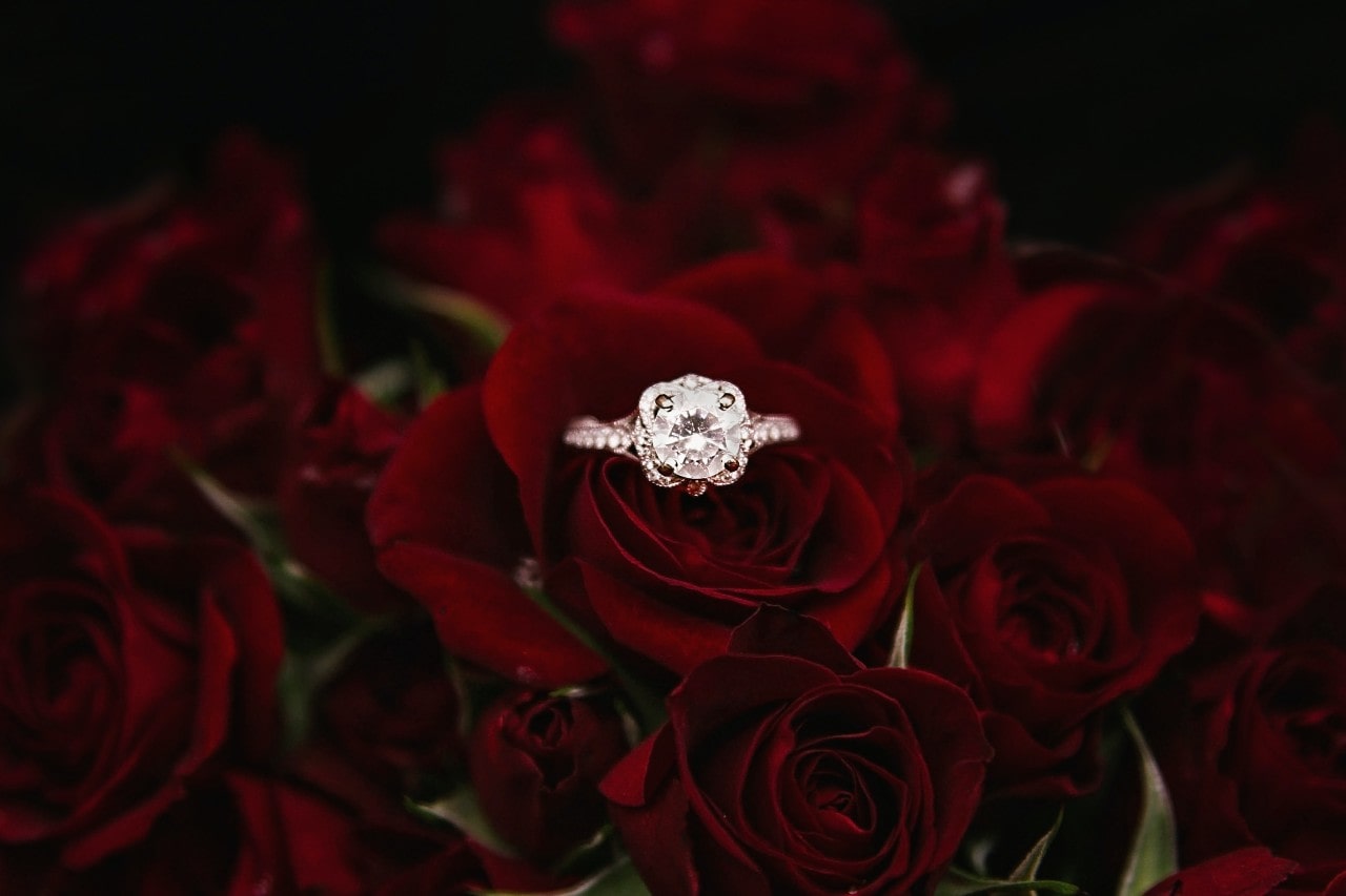 An intricate diamond engagement ring sitting in the middle of a bouquet of red roses