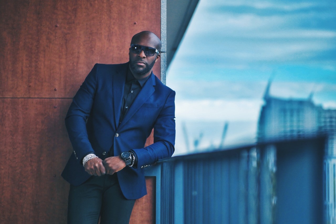 A well-dressed man standing in an urban landscape, wearing a suit and luxury watch.