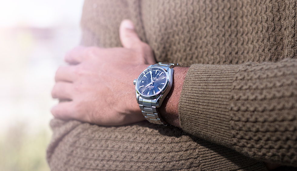 A man stands outside in a cardigan wearing a stainless steel watch.