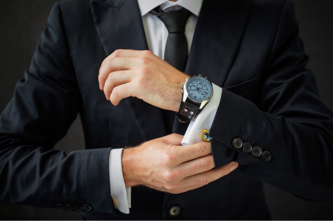 A businessman adjusts his cuff, while wearing a light blue dial watch.