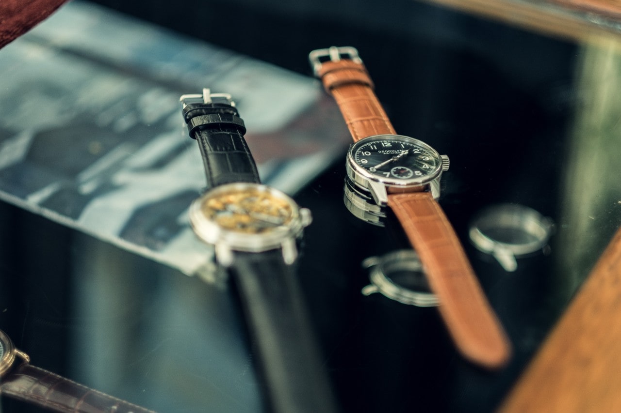 Two watches with an alligator leather watch strap on a coffee table.