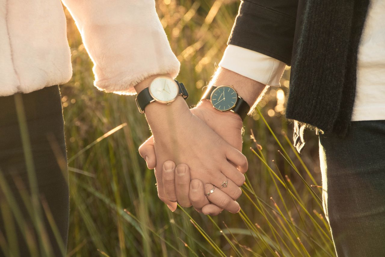 A couple holding hands while walking in an overgrown field.