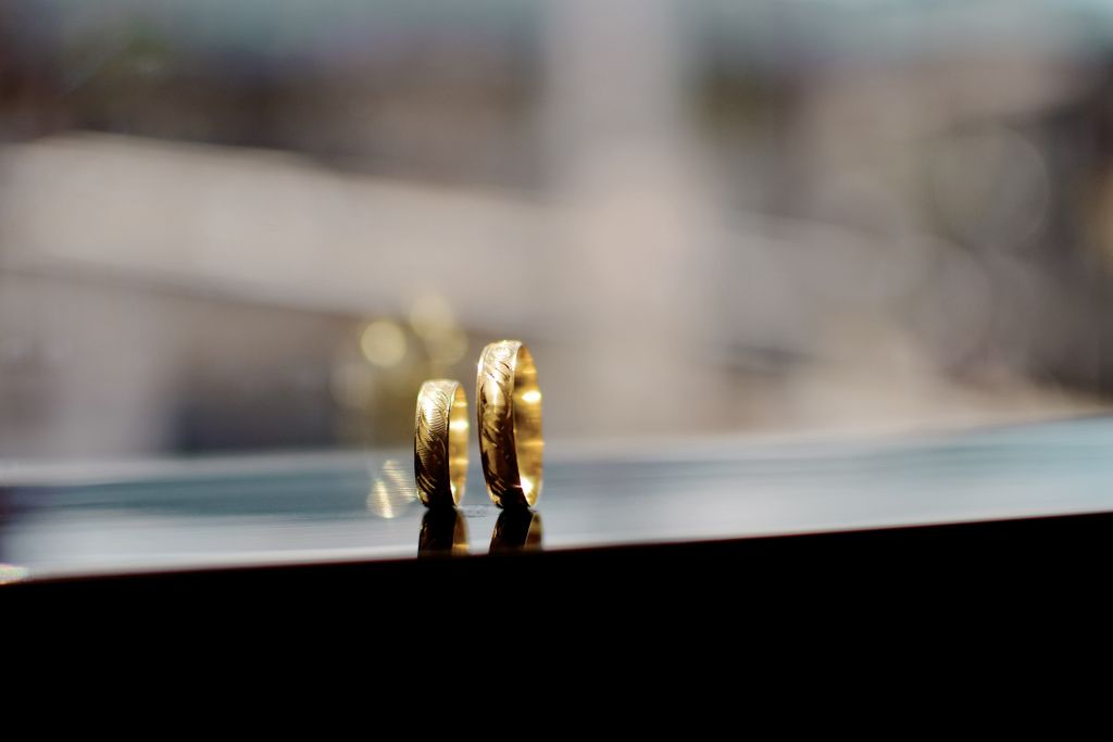 A pair of gold men’s wedding bands sit on a window sill.