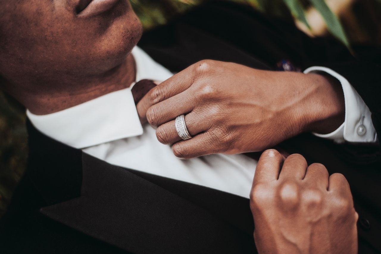 A man adjusts his tie, showing off his platinum and diamond wedding band.