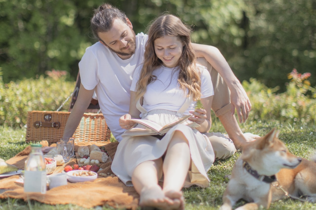 a man and woman having a picnic, wearing white, and reading a book together