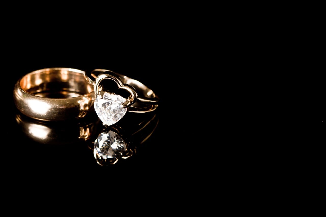 a yellow gold wedding band and engagement ring set against a black background