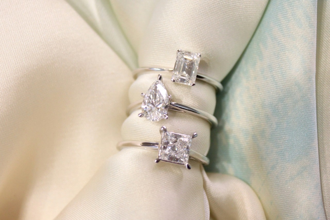 three silver solitaire engagement rings stacked on a piece of ivory fabric