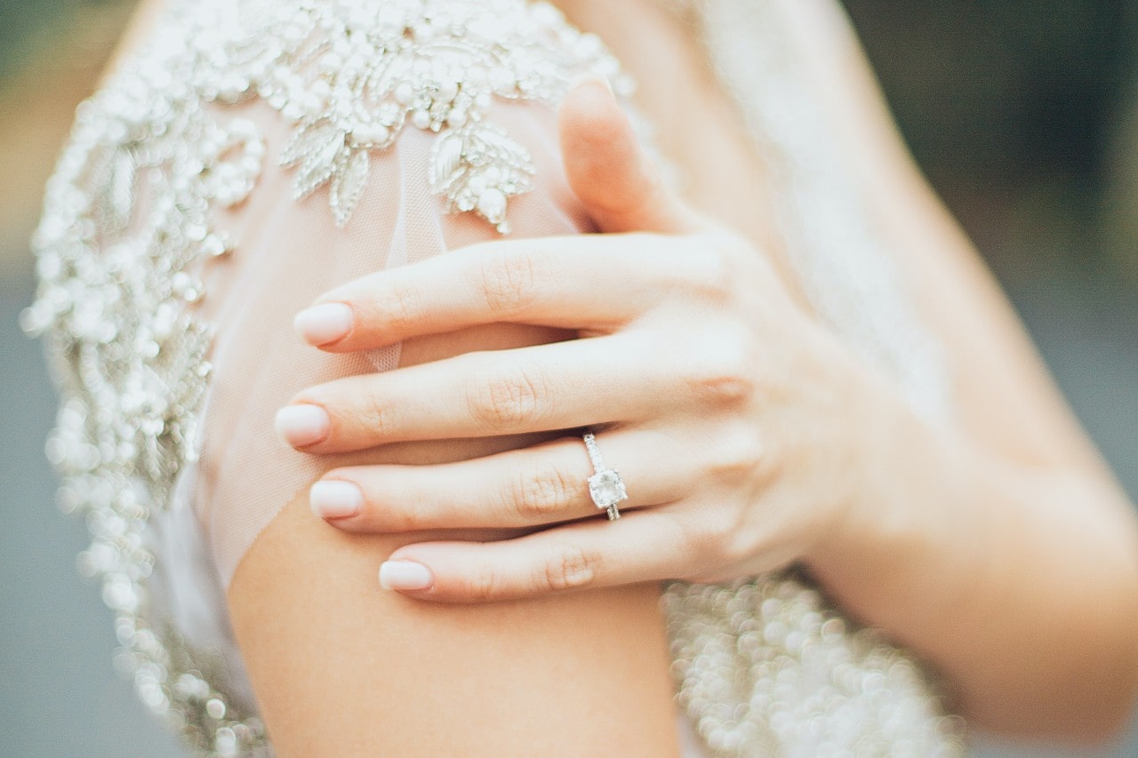 A bride rests her hand on her shoulder while wearing a side stone ring.