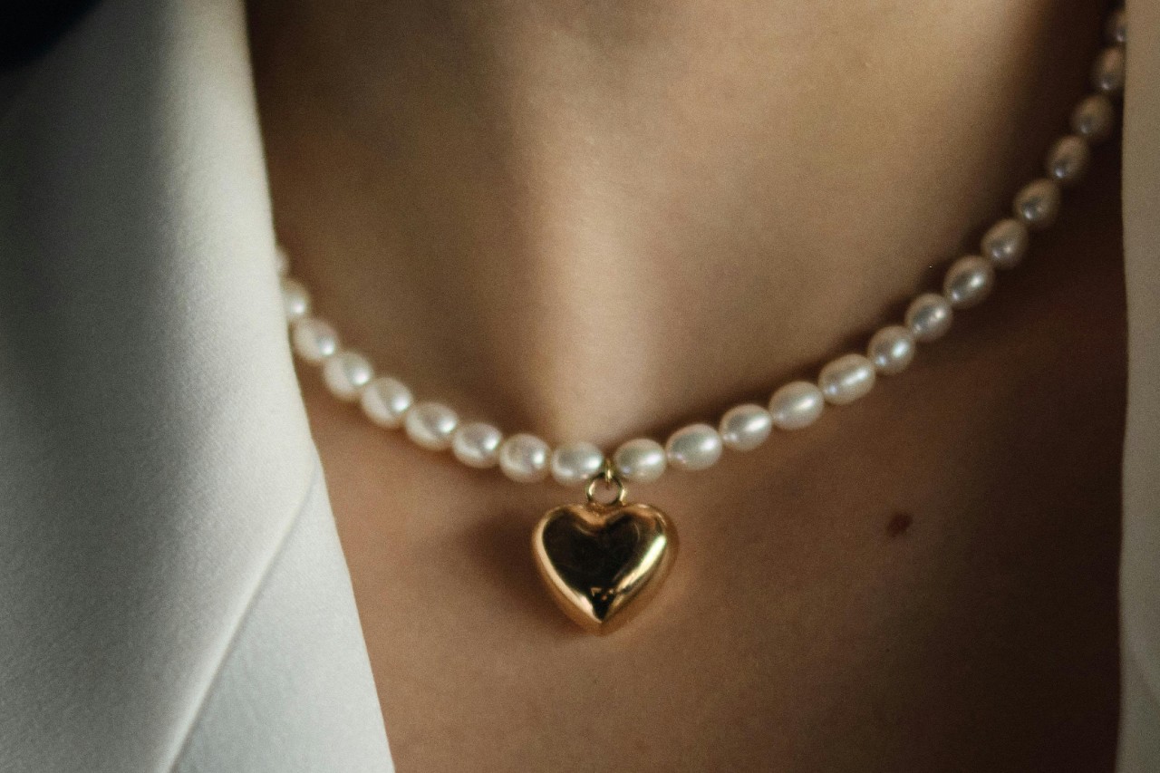 close up image of a woman’s neckline adorned with a pearl necklace and a yellow heart pendant