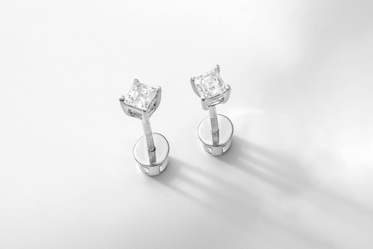 a pair of princess cut diamond stud earrings on a white surface