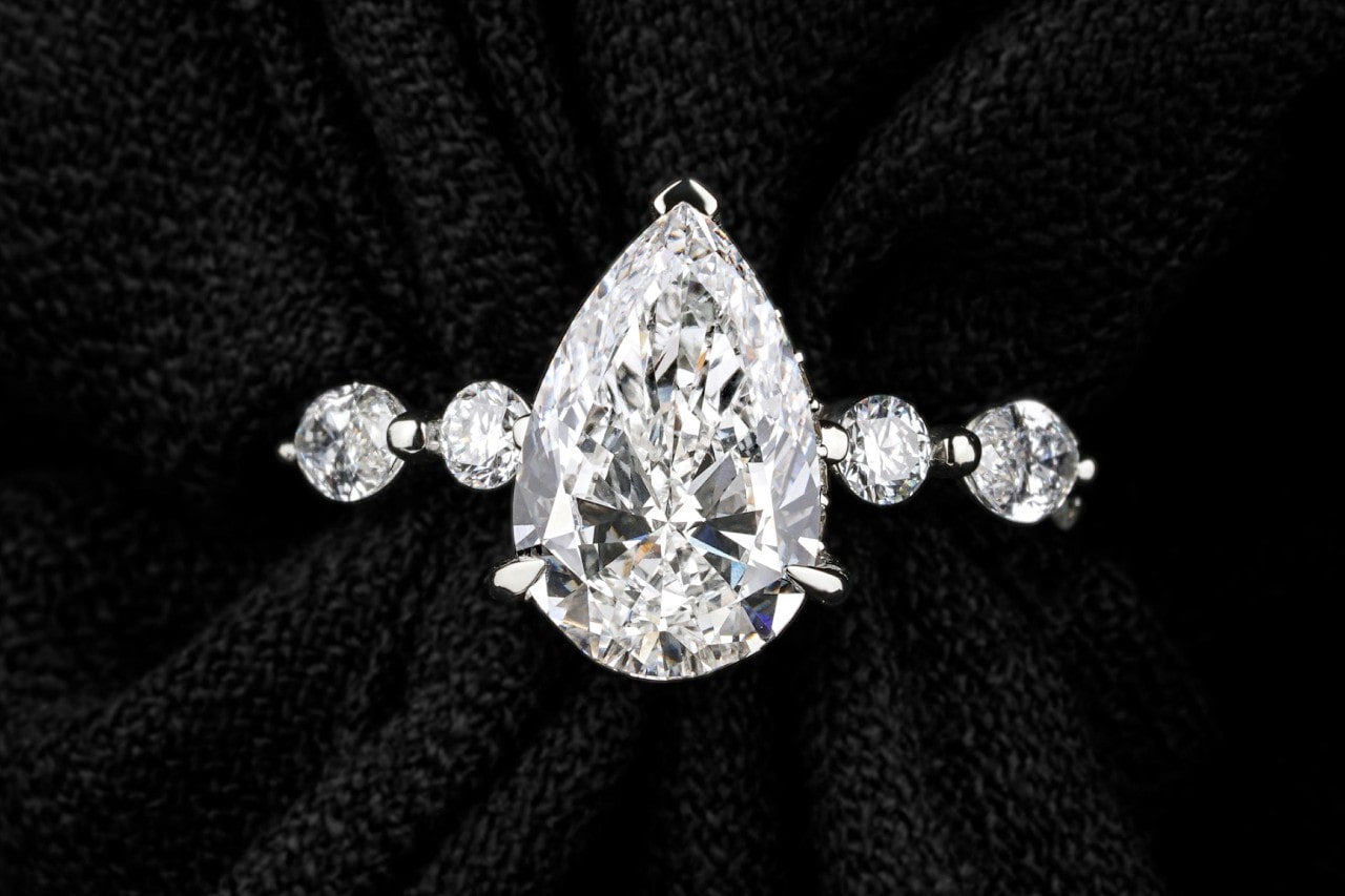 A close-up of an engagement ring with a pear shape center stone and round cut side stones.