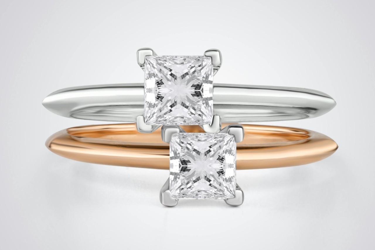 Two solitaire, princess cut engagement rings, one in white gold, the other in rose gold, stacked one on top of the other.