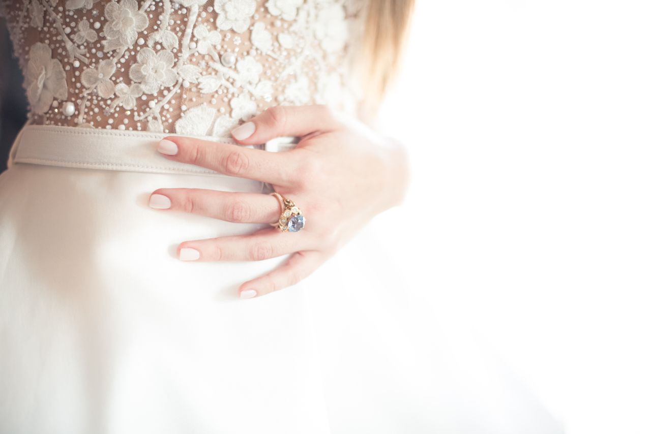 A bride rests her hand on her waist, wearing a gemstone engagement ring.