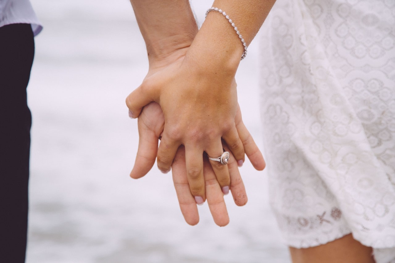 A bride-to-be holds hands with her partner, showing off her halo ring.