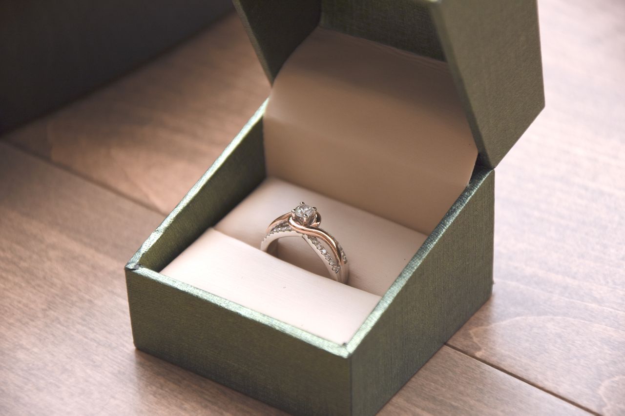 A two-tone split shank engagement ring in a ring box on a wooden table.